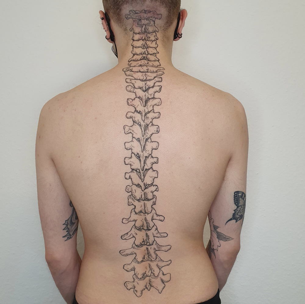 Schwarzes Holzschnitt Tattoo einer Wirbelsäule. Das Tattoo verläuft anatomisch darüber, wo die Wirbelsäule ist.