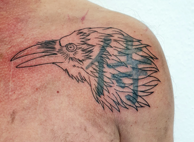 Cover-up Vogel Tattoo: ein Krähenkopf wurde über ein Schriftzeichen, dass gecovert werden soll, platziert.