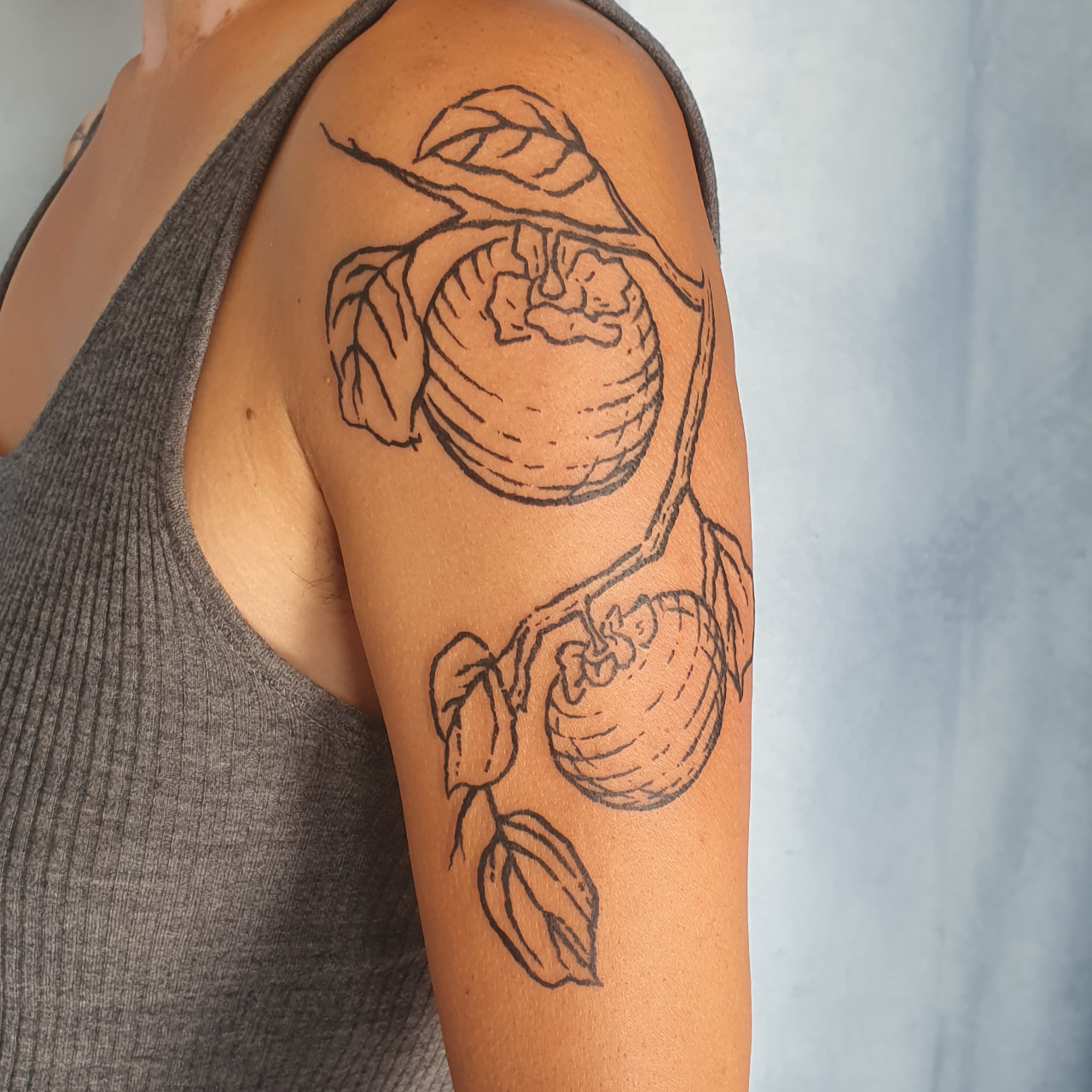 Holzschnitt Tattoo eines Kaki Asts, an dem zwei Kaki Früchte hängen. Schwarze Obst Tätowierung.