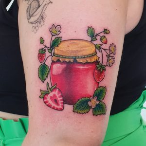 Colorful tattoo of red jam jar with yellow lid surrounded by strawberries.