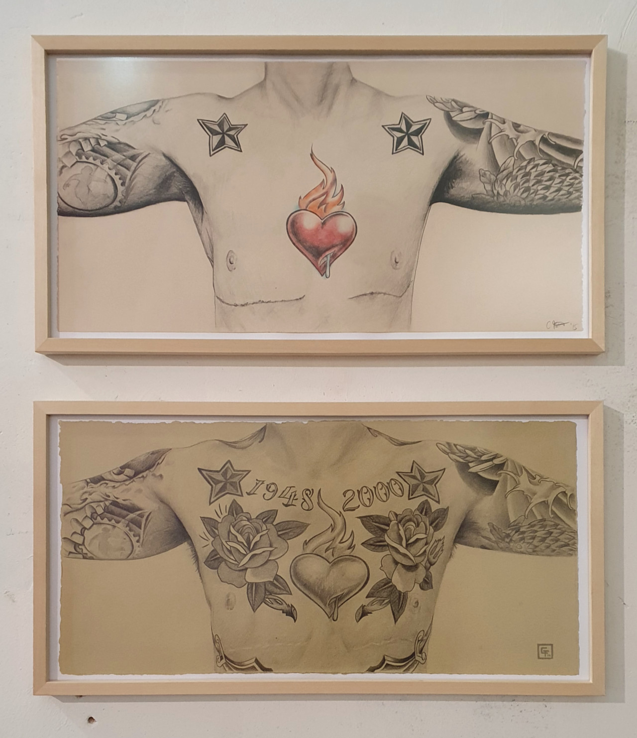 Picture of two framed pencil drawings of a torso with tattoos and scars